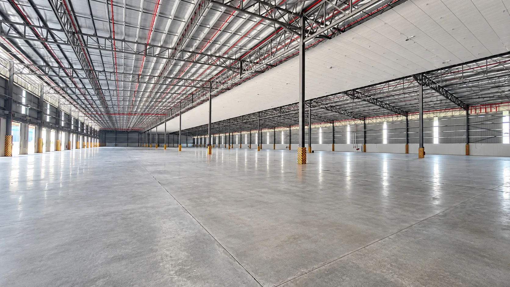 Inside an empty bonded warehouse in Johor, with a steel roof structure, loading doors and a clear concrete floor