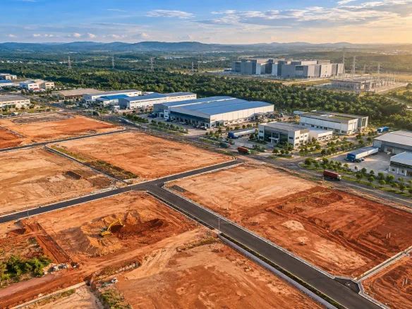 Aerial view of cleared industrial land plots for sale in Johor, with factories and a data centre campus in the background