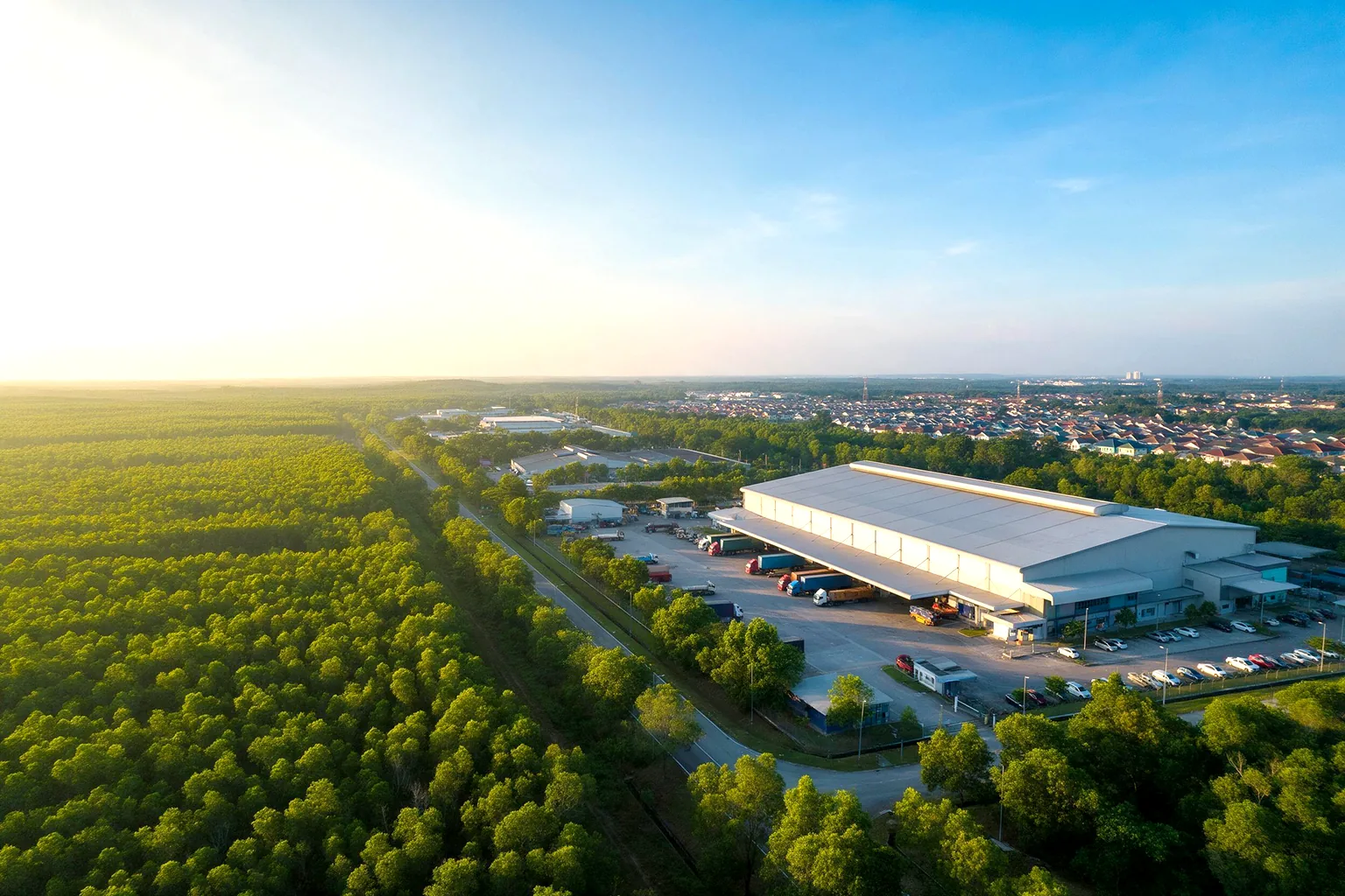 Aerial view of a factory in Johor surrounded by green trees, with a housing area in the distance